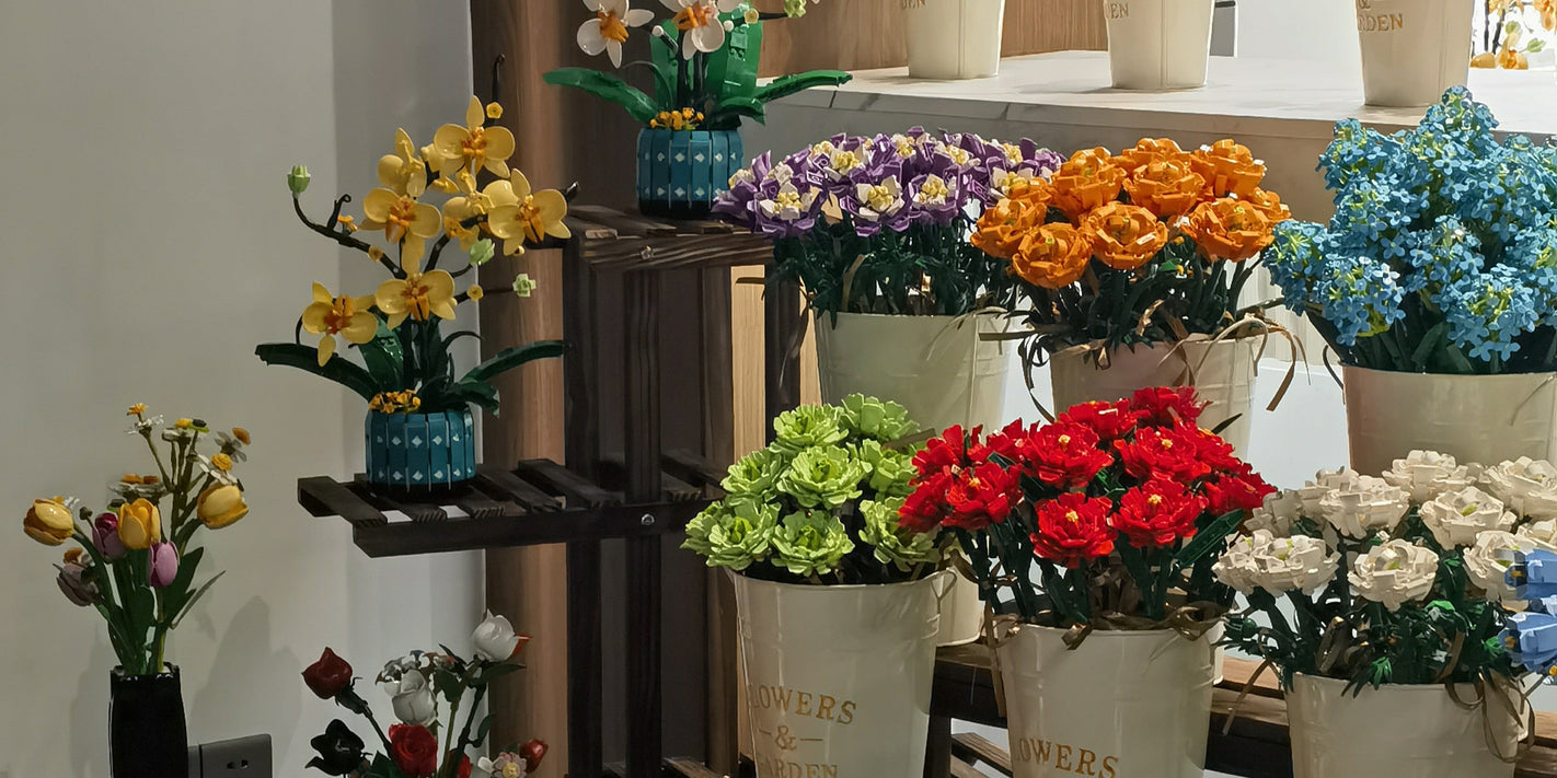 A diverse display of Mavirea building block flowers, including orchids and roses, arranged in "Flowers & Garden" buckets, offering a wide selection for home decoration and gifts.
