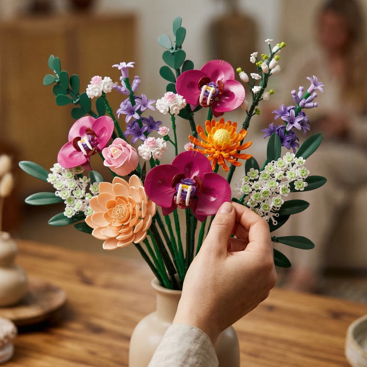 A close-up of a Mavirea building block floral arrangement resting on a rustic wooden table in a warm, sunlit room. The detailed textures of the orange gerberas and lush green stems emphasize its high-quality design as a maintenance-free interior accent.
