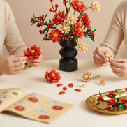 Two people assembling a Mavirea building block flower bouquet on a table, featuring vibrant red and cream blooms—a perfect creative activity and home decor piece.