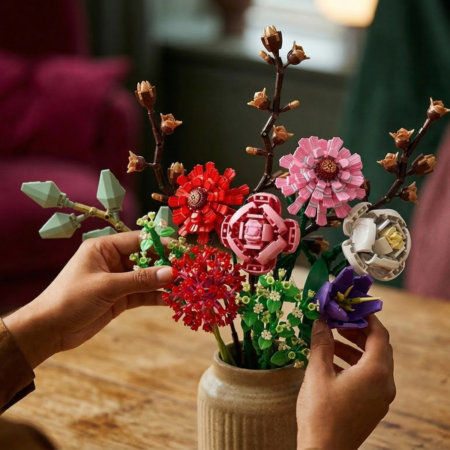 Close-up of hands arranging a diverse Mavirea floral bouquet—featuring red, pink, and purple building block blooms—into a ceramic vase for an elegant, eternal home display.