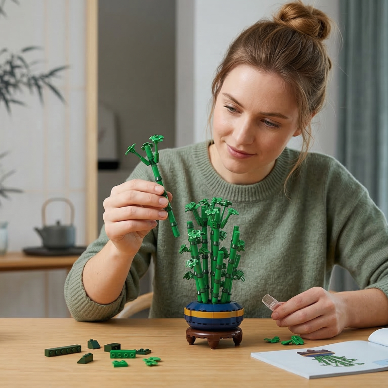A woman in a green sweater enjoys the DIY process of assembling the Mavirea Gourd Bamboo Bonsai, with building blocks and the instruction manual spread out on a wooden table.