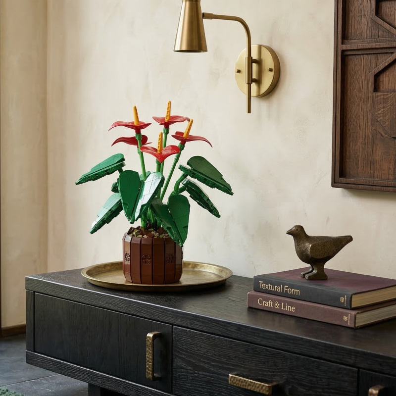 A vibrant Mavirea Anthurium Bonsai building set styled on a sleek dark sideboard, paired with a gold tray and minimalist decorative books, showcasing its bold red petals as a high-end home decor accent.