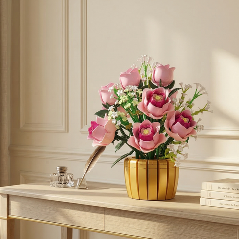 A Mavirea Pink Rose Potted Plant building set in a radiant gold vase, styled on a classic wooden desk next to a feather quill and ink bottle, perfect for sophisticated home office decor.