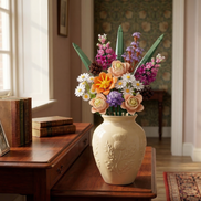 The Whispering Pines Floral bouquet by Mavirea styled in a cream-colored thistle vase on a vintage wooden desk, showcasing it as a sophisticated, maintenance-free 