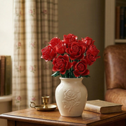 A Mavirea Red Roses Bouquet building set in an embossed white ceramic vase, styled on a warm wooden table next to a brass candle holder and a vintage book for a classic home decor feel.