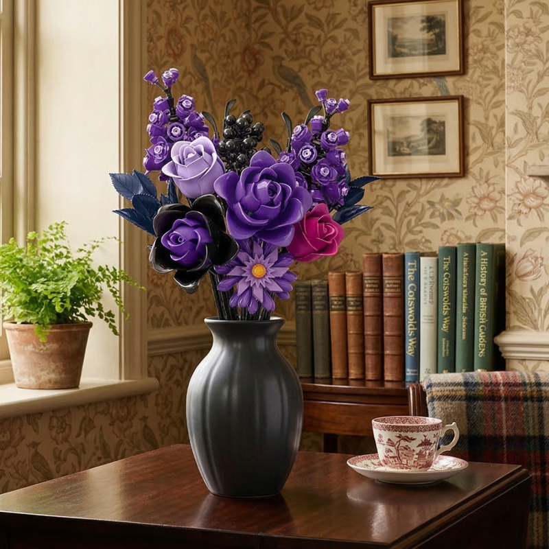 A classic, cozy home setting featuring the Mavirea Purple Rose Whisper building block bouquet in a matte black fluted vase, styled on a wooden table alongside a vintage teacup and a collection of books against floral wallpaper.