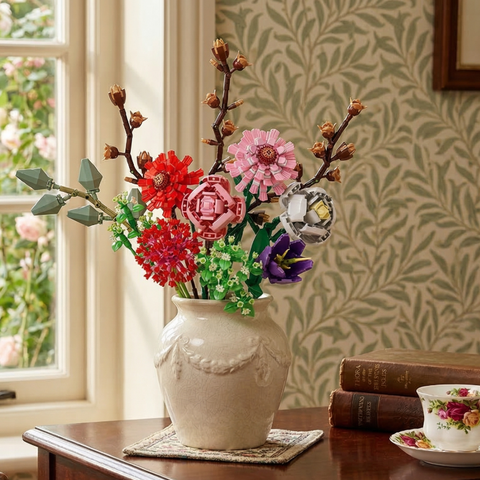 Mavirea "The Pretty In Pink" building block bouquet in an ornate white vase, styled with a floral teacup and books for a bright, cozy home decor accent.