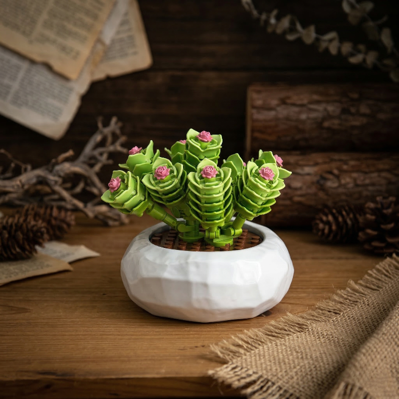 A Mavirea green tiered succulent with pink flower accents in a white geometric pot, set against a rustic wooden background for a cozy, nature-inspired home vibe.